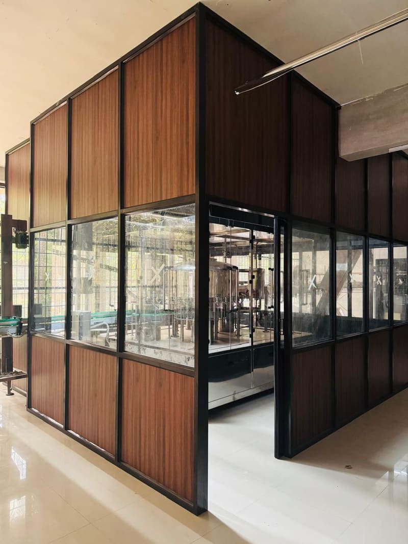 The enclosed bottling room seen through its glazed partition, with filling equipment inside.