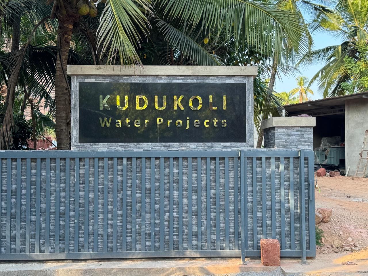 The stone-clad entrance sign reading Kudukoli Water Projects beside the site gate.