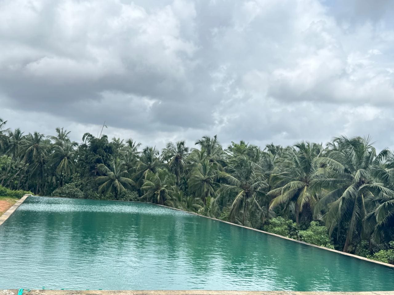 The reservoir at Kudukoli under a heavy monsoon cloudscape, coconut palms along the far bank.